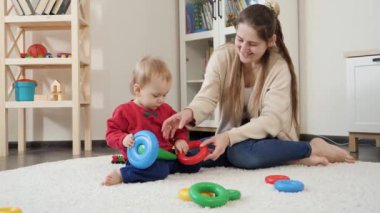 Evde yumuşak halıya çocuk oyuncağı kulesi inşa eden mutlu bir anne. Bebek gelişimi, çocuk oyunları, eğitim ve öğrenim