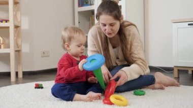 Küçük oğluna renkli oyuncak piramidi yapmayı öğreten genç bir anne. Bebek gelişimi, çocuk oyunları, eğitim ve öğrenim