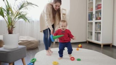 Bebek gibi gülümseyen mutlu çocuk, elinde oyuncaklar, oturma odasında halıda yürümeyi öğreniyor. Bebek gelişimi, aile oyunları, ilk adımlar, ebeveynlik ve bakım.