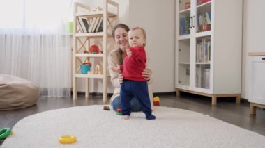 Annesinin ilk adımlarını attığı ve kameraya doğru yürüdüğü sevimli bir erkek bebek. Bebek gelişimi, aile oyunları, ilk adımlar, ebeveynlik ve bakım.