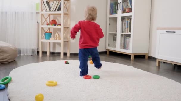 小さな赤ちゃんの男の子はカーペットの上を歩くことを学び カラフルなおもちゃを拾う 赤ちゃんの発達 家族で遊ぶゲーム 第一歩を踏み出す 親とケア — ストック動画