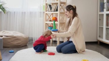 Güzel gülümseyen anne, küçük oğlunun oyuncak kulesini kurmasına yardım ediyor. Bebek gelişimi, çocuk oyunları, eğitim ve öğrenim