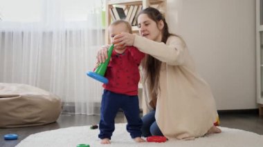 Küçük bebek renkli oyuncak piramidini oturma odasında monte ettikten sonra tezahürat yapıyor. Bebek gelişimi, çocuk oyunları, eğitim ve öğrenim