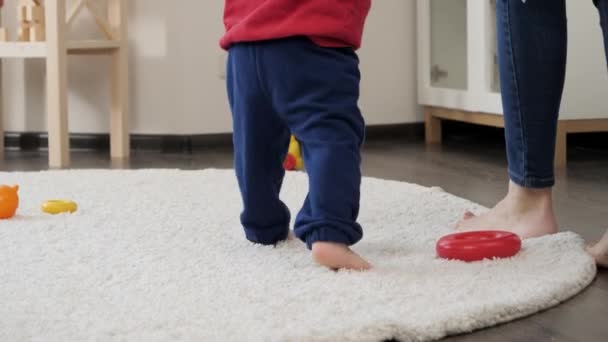 小さな赤ちゃんの足の閉鎖生活室で柔らかいカーペットの上で母親と一緒に歩くことを学ぶ 赤ちゃんの発達 家族で遊ぶゲーム 第一歩を踏み出す 親とケア — ストック動画