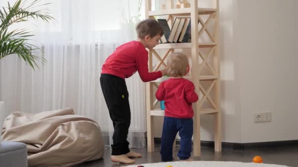 大男孩帮助他的小弟弟从客厅的高架子上拿玩具 儿童教育 婴儿发展 家庭游戏的概念 — 图库视频影像
