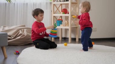 Küçük çocuk renkli oyuncak piramidini ağabeyiyle oturma odasında birleştiriyor. Çocuk eğitimi kavramı, bebek gelişimi, aile oyunları