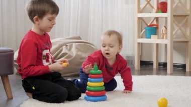 Oturma odasındaki halının üzerine oyuncak kule kurduktan sonra gülümseyen ve tezahürat yapan iki küçük çocuk. Çocuk eğitimi kavramı, bebek gelişimi, aile oyunları