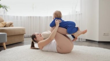 Yerde uzanan ve küçük oğluyla oynayan mutlu genç bir kadın. Aile sağlığı, aktif yaşam tarzı, ebeveynlik ve çocuk gelişimi.