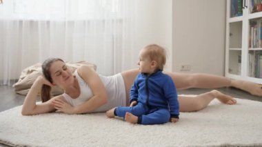 Güzel, gülümseyen bir kadın, oğluyla halının üzerinde uzanıyor ve spor yapıyor. Aile sağlığı, aktif yaşam tarzı, ebeveynlik ve çocuk gelişimi.