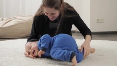 Genç, şefkatli bir anne, oturma odasında küçük oğluna jimnastik yapıyor ve esneme egzersizleri yapıyor. Aile sağlığı, aktif yaşam tarzı, ebeveynlik ve çocuk gelişimi.