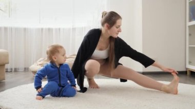 Küçük oğlu olan genç ve güzel bir kadın evde halının üzerinde esneme ve spor yapıyor. Aile sağlığı, aktif yaşam tarzı, ebeveynlik ve çocuk gelişimi.