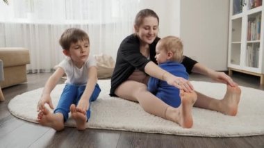 Yavrusu ve büyük oğluyla birlikte evde halı üzerinde esneme ve spor yapıyor. Aile sağlığı, aktif yaşam tarzı, ebeveynlik ve çocuk gelişimi.