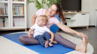 Genç bir kadın evde küçük oğluyla esniyor ve spor yapıyor. Sağlık, spor, çocuk bakımı ve çocuk gelişimi kavramı.