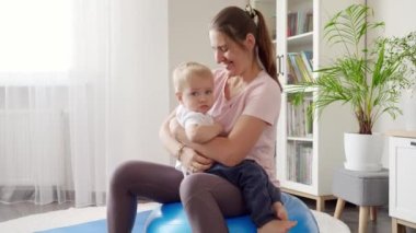 Gülümseyen genç bir kadın üzgün oğlunu tutuyor ve evde spor yapıyor. Evde sağlık, spor ve yoga kavramı.