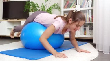 Spor salonunda yatan ve yuvarlanan gülümseyen genç bir kadın. Evde sağlık, spor ve yoga kavramı