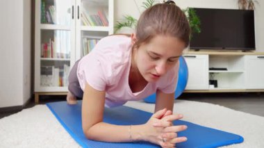 Oturma odasındaki jimnastik paspasının üzerinde duran konsantre genç kadın portresi. Evde sağlık, spor ve yoga kavramı