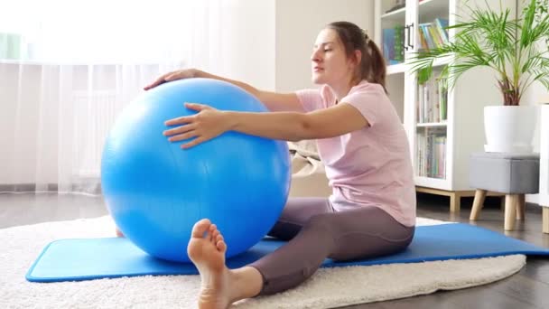 漂亮的年轻女子坐在健身垫上 用适形球做伸展运动 家庭保健 体育和瑜伽的概念 — 图库视频影像