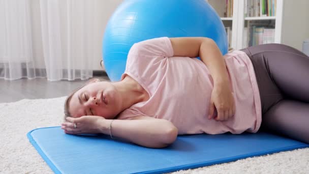 疲れた若い女性がフィットネスマットに横たわっており 自宅でのハードトレーニングの後 ほとんど呼吸 自宅での医療 スポーツ ヨガの概念 — ストック動画