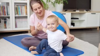 Mutlu gülümseyen anne evde minderdeki 1 yaşındaki oğluyla jimnastik ve spor yapıyor. Sağlık, spor, çocuk bakımı ve çocuk gelişimi kavramı