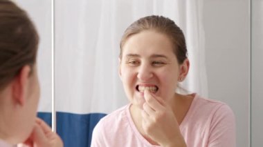 Güzel, gülümseyen bir kadın aynadaki yansımasına bakıyor ve diş plağını ovuyor. Diş sağlığı, ağız kontrolü ve ağız temizliği kavramı