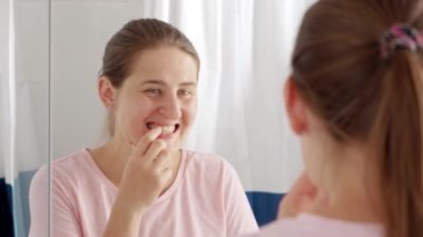 Banyodaki aynada dişlerini ve dilini plaka için kontrol eden genç bir kadının portresi. Diş sağlığı, ağız kontrolü ve ağız temizliği kavramı