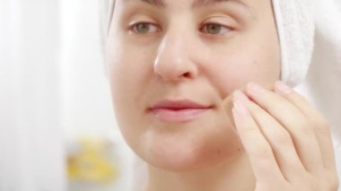 Banyo havlusu giymiş genç bir kadının yüzüne yumuşak süngerle kozmetik sürüşü. Güzel kadın kavramı, evde makyaj, cilt bakımı ve yerli güzellik endüstrisi..