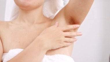 Banyodaki aynada duran genç bir kadının kollarının altında uzayan uzun siyah saçları. Güzel kadın kavramı, doğal güzellik, kadınlık ve vücut kılları.