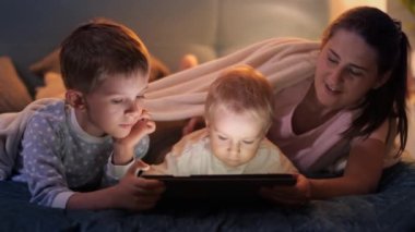 Annesi ve ağabeyi ile birlikte yatmadan önce tablet bilgisayarda oyun oynayan tatlı bir erkek bebek. Ailenin birlikte vakit geçirmesi, ebeveynlik, mutlu bir çocukluk ve eğlence.