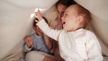 Mutlu aile battaniyenin altında saklanıyor ve el feneriyle oynuyor. Ailenin birlikte vakit geçirmesi, ebeveynlik, mutlu bir çocukluk ve eğlence.