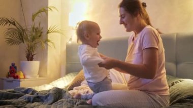 Genç bir anne ve küçük oğlu yatakta oynayıp zıplıyorlar. Ailenin birlikte vakit geçirmesi, ebeveynlik, mutlu bir çocukluk ve eğlence.