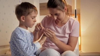 İlgili genç anne, oğluna tırnaklarını kesiyor. Yatak odasında pijama giyiyor. Ebeveyn, çocuk hijyeni ve sağlık sigortası yapıyor.