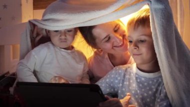 Geceleri battaniyenin altında oturup tablet bilgisayarda çizgi film izleyen mutlu bir aile. Ailenin birlikte vakit geçirmesi, aletli çocuklar, ebeveynlik, mutlu bir çocukluk ve eğlence.