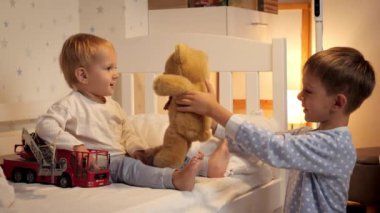 İki çocuk gece yatakta oyuncak ayı ve oyuncak arabayla oynuyor. Ailenin birlikte vakit geçirmesi, ebeveynlik, mutlu bir çocukluk ve eğlence.