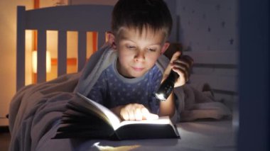 Pijama giymiş, elinde fener tutan ve ilginç kitaplar okuyan sevimli bir çocuk portresi. Çocuk eğitimi, gelişme, gizlilik, mahremiyet, kitap okuma