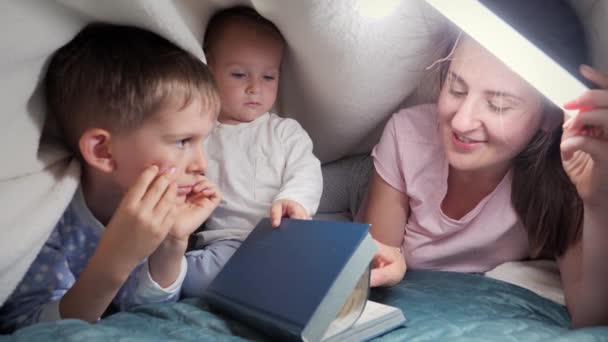 Усміхнена Жінка Двома Синами Лежить Під Ковдрою Читає Книгу Про — стокове відео