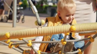 Örümcek ağında sallanan sevimli sarışın bebek çocuk parkta sallanıyor. Çocuklar dışarıda oynuyor, çocuklar dışarıda, yaz tatili ve tatil.