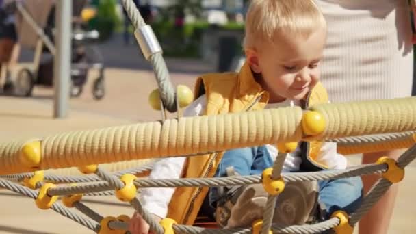 可爱的金发碧眼的小男孩在操场上用蜘蛛网绳荡秋千 儿童在室外玩耍 儿童在室外玩耍 暑假和假期 — 图库视频影像
