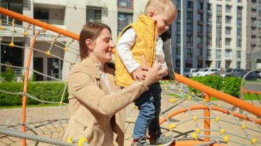Genç bir anne, oğlunu destekliyor. Çocuk parkında dengede duruyor. Çocuklar dışarıda oynuyor, çocuklar dışarıda, yaz tatili ve tatil.