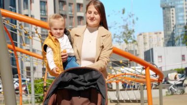 Güzel bir anne bebeğini kucağında tutuyor sokakta yürüyor ve bebek arabasını itiyor. Mutlu ebeveynlik, ailenin birlikte zaman geçirmesi, çocuklar ve ebeveynler dışarıda.