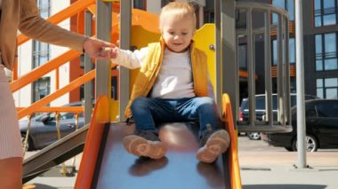 Annesinin elini tutan ve oyun parkında kaydırak süren tatlı bir çocuk. Mutlu ebeveynlik, ailenin birlikte zaman geçirmesi, çocuklar ve ebeveynler dışarıda.
