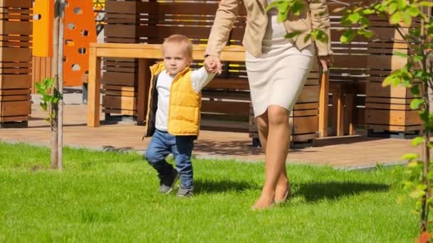 可爱的小男孩和妈妈在绿草草坪上慢慢地走着 户外儿童 大自然中的儿童 户外玩耍的婴儿 — 图库视频影像