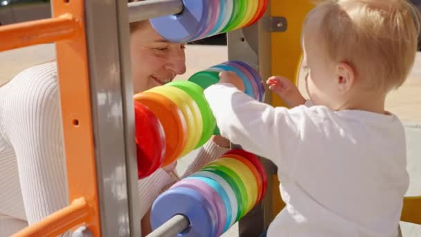 遊び場でカラフルなそろばんで遊んでいる赤ちゃんの男の子と幸せな笑顔の母親 子供の発達子供の教育赤ちゃんの学習 — ストック動画
