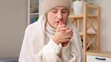 Isıtma problemleri yüzünden evinde şapkalı ve örgü kazaklı genç bir kadın donuyor. Enerji krizi, yüksek faturalar, ekonomi ve aylık faturalardan tasarruf kavramı