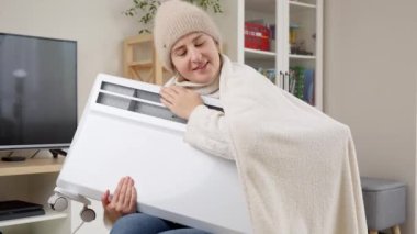 Şapkalı bir kadın evinde ısıtmasız elektrikli ısıtıcı tutuyor. Enerji krizi, yüksek faturalar, ekonomi ve aylık faturalardan tasarruf kavramı