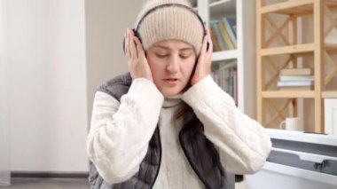 Soğuk bir dairede atkı ve kulak ısıtıcı takan genç bir kadın. Enerji krizi, yüksek faturalar, ekonomi ve aylık kamu hizmetleri ödemelerinde tasarruf kavramı