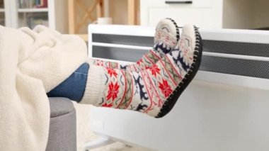 Elektrikli ısıtıcıda battaniyenin altında sıcak çorapların içinde ısınan ayaklar. Enerji krizi, yüksek faturalar, ekonomi ve aylık kamu hizmetleri ödemelerinde tasarruf kavramı