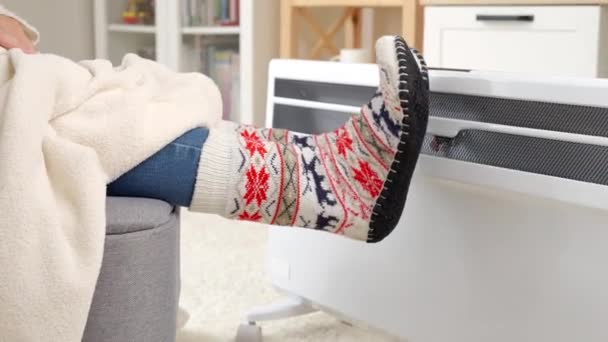 电暖炉里穿针织袜子暖脚的女人的衣服 能源危机的概念 高额费用 经济和节省每月公用事业付款 — 图库视频影像