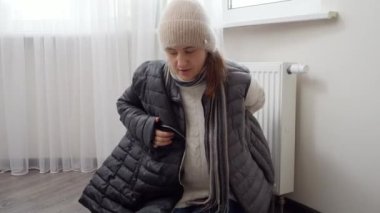 Evde donan bir kadın radyatörde sıcak bir palto giyiyor. Enerji krizi, yüksek faturalar, bozuk ısıtma sistemi, ekonomi ve aylık kamu hizmetleri ödemelerinde tasarruf kavramı.