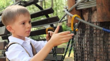 Dışarıdaki kaya parkına tırmanırken güvenlik halatı kancasını kenetleyen küçük çocuğun portresi. Aktif çocukluk, sağlıklı yaşam tarzı, açık havada oynayan çocuklar, doğadaki çocuklar.