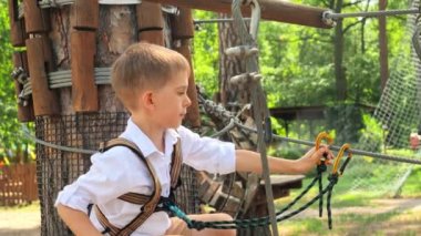 İzci kampında eğlenirken ip köprüde yürüyen küçük şirin bir çocuğun portresi. Aktif çocukluk, sağlıklı yaşam tarzı, açık havada oynayan çocuklar, doğadaki çocuklar.